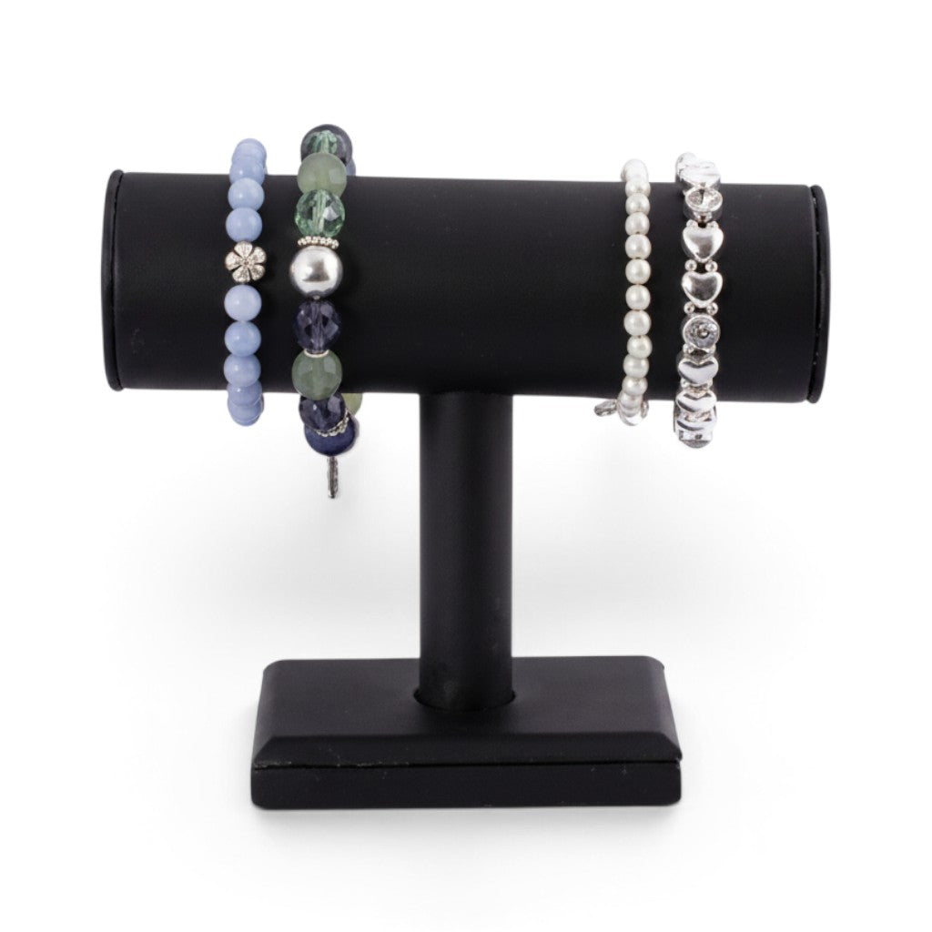SuperSellerS svartur kunstleður T-stong armbandsdisplaystandari við fýra ymiskum perlu- og silvurarmbondum.